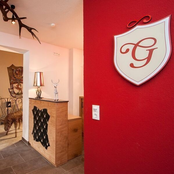 A reception area with a wooden desk, a lamp, and a coat rack. A coat is hanging on the wall. - Apartmenthaus Gurglhof (Soelden)