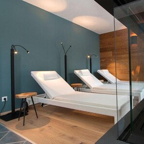 A modern spa room with two white massage tables, wooden flooring, and tall floor lamps. - Apartmenthaus Gurglhof (Soelden)