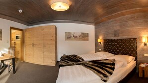 A cozy room with a bed, a desk with a chair, a wooden wardrobe, and wall-mounted lights. - Apartmenthaus Gurglhof (Soelden)