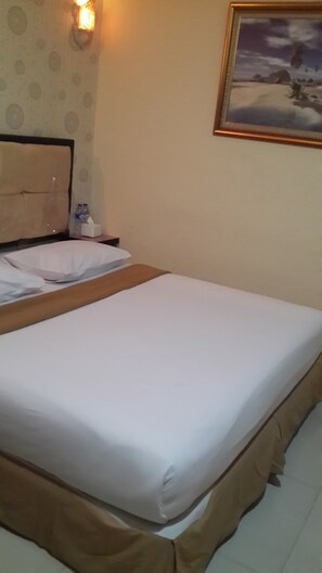 A neatly made bed in a hotel room with a headboard, a wall-mounted light, and a framed picture on the wall.