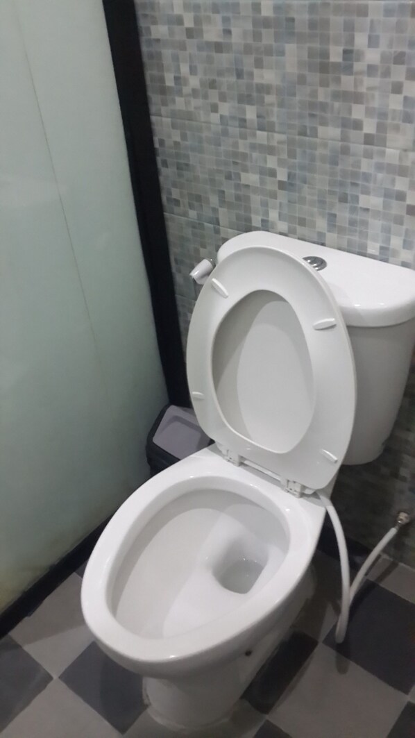 A white toilet with a closed seat in a bathroom with tiled walls and a checkered floor. - Hotel California (Jakarta)