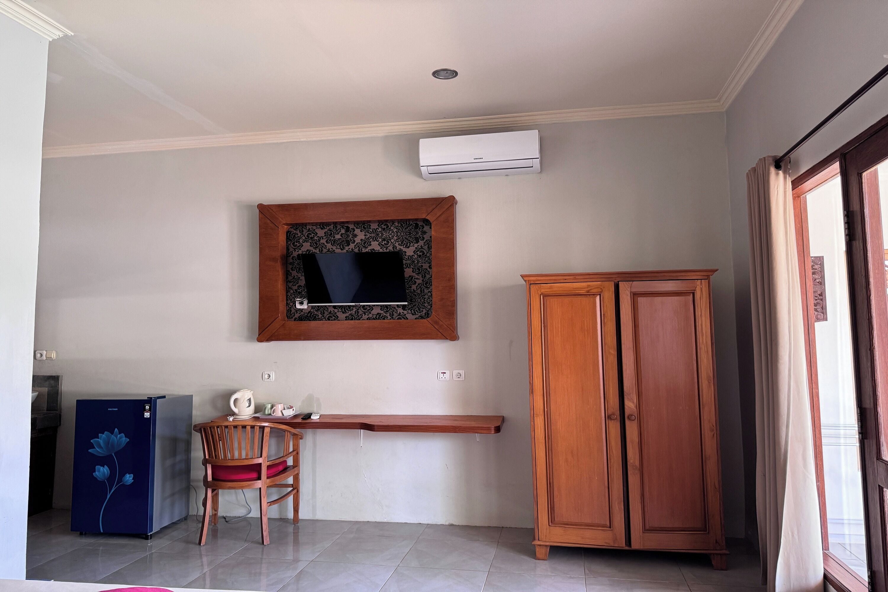 A room with a wooden cabinet, a small table with a chair, a blue refrigerator, and a mounted air conditioner.