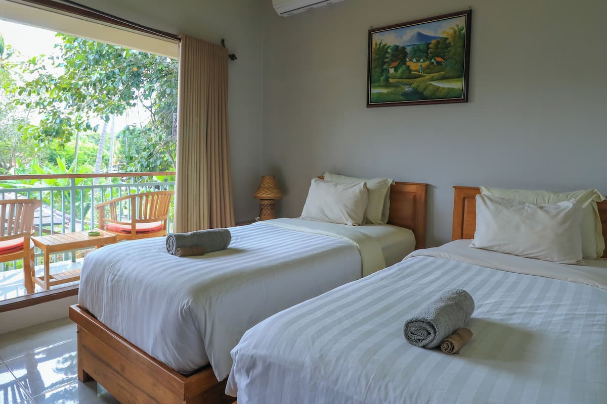 A hotel room with two beds, a balcony with chairs, and a painting on the wall.
