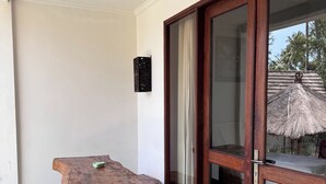 Een houten tafel en bank staan in een ruimte met een betegelde vloer en een schuifdeur van glas.
