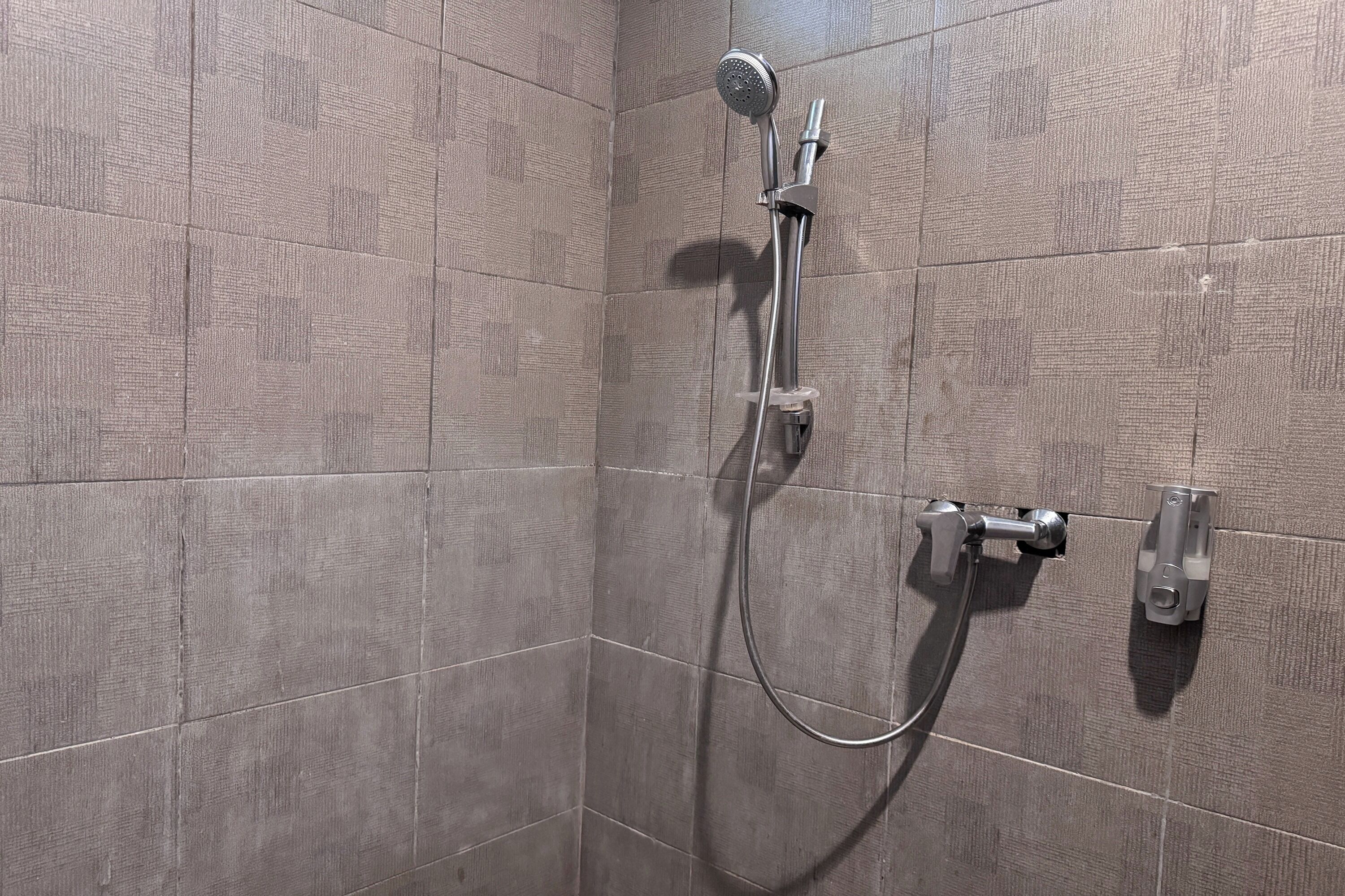 Un área de ducha con un cabezal de ducha de mano y una llave de pared.