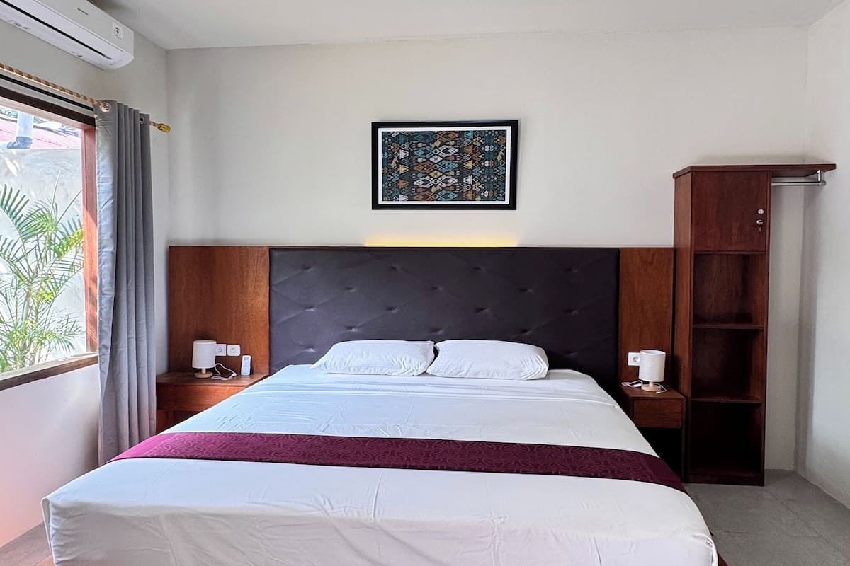A modern hotel room with a large bed, a headboard, a nightstand, a bedside table, a wardrobe, and a window with curtains.