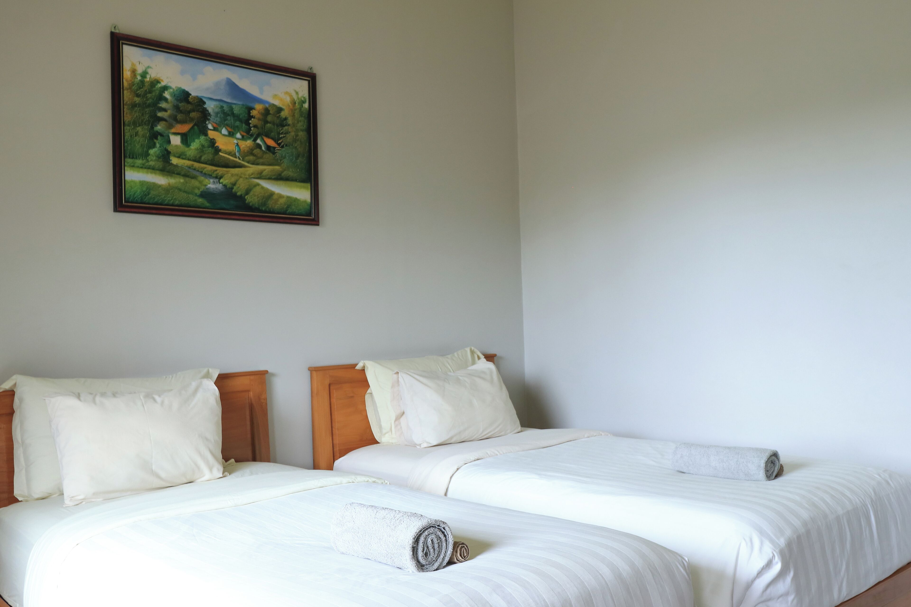 A hotel room with two beds, white bedding, and a painting of a landscape on the wall.