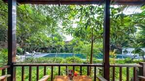 A wooden table with a vase of flowers, a red cushion, and a view of a swimming pool surrounded by lush greenery. - An Nhien Retreat Phu Quoc (Phu Quoc)