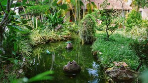 A serene garden with a pond, lush greenery, and a traditional house in the background. - An Nhien Retreat Phu Quoc (Phu Quoc)