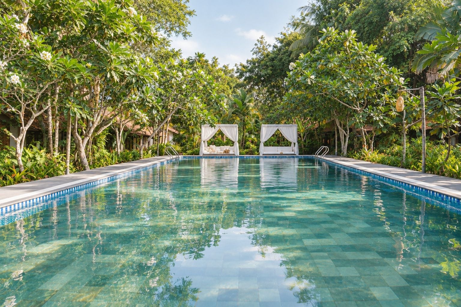 A clear swimming pool surrounded by lush greenery and two white canopy beds.