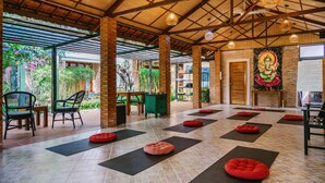 A spacious indoor area with a high ceiling, wooden beams, and a brick wall with a mural. There are exercise mats and red cushions on the floor, and a table with chairs in the background. - An Nhien Retreat Phu Quoc (Phu Quoc)