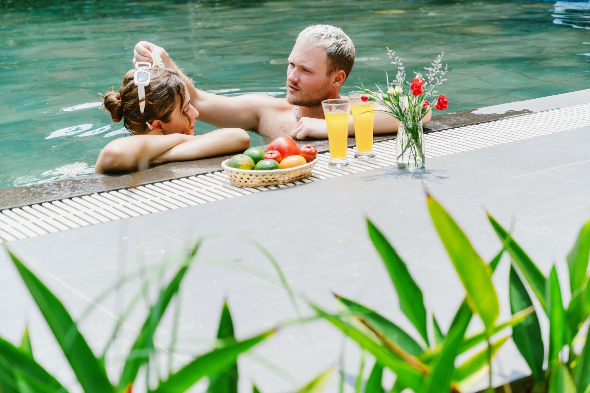 A poolside setting with a table featuring a fruit basket, drinks, and flowers.