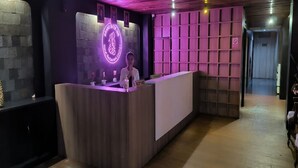 Un mostrador de recepción con un letrero de neón, una recepcionista y una pared con diseño de cuadrícula.