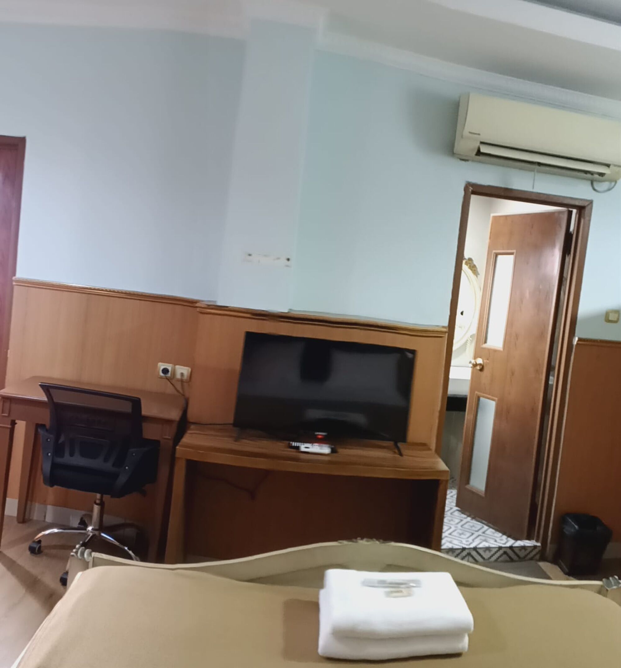 A hotel room with a bed, a desk with a television, a chair, and a door.