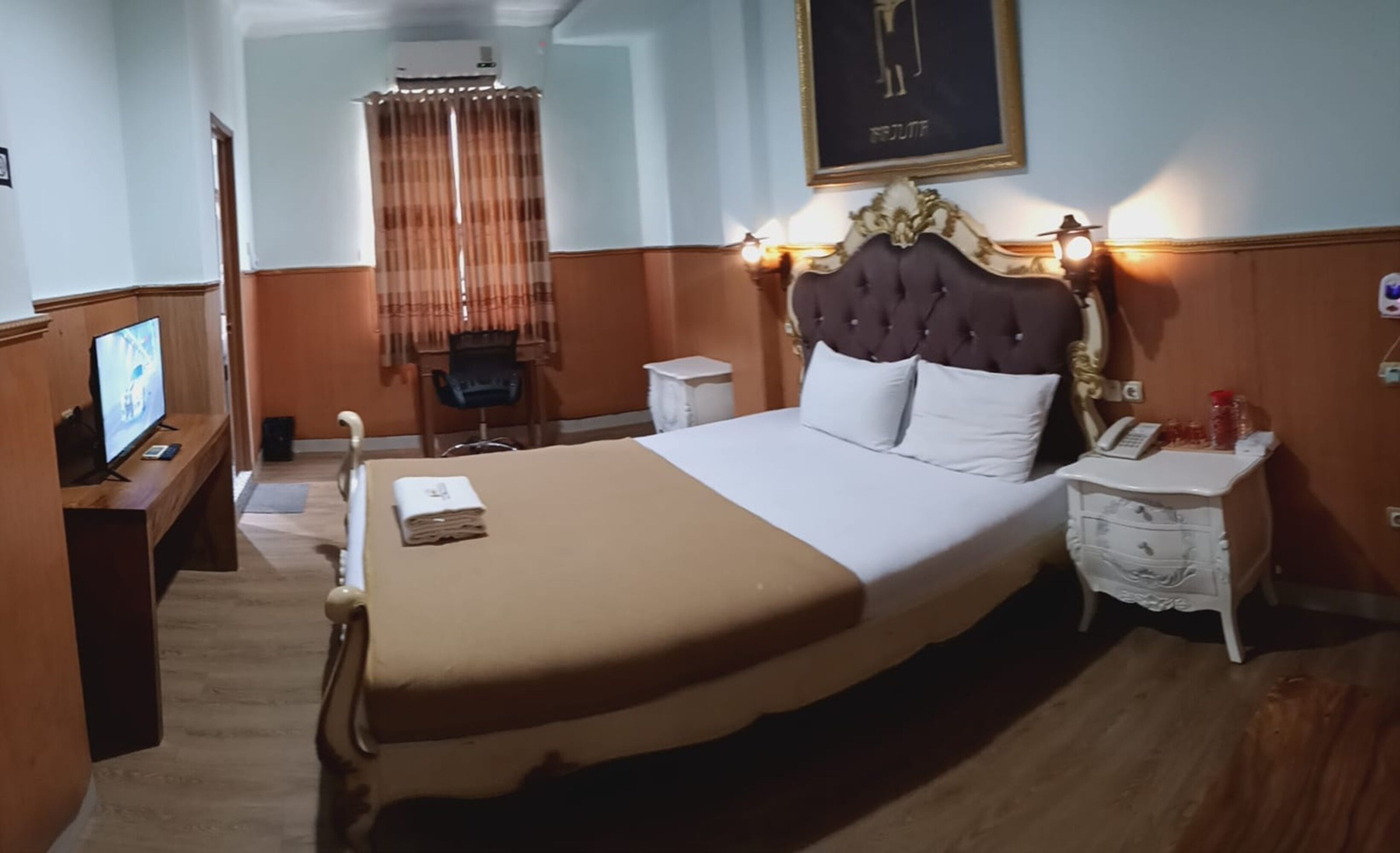 Une chambre d’hôtel avec un grand lit, une table de chevet avec une lampe, une chaise, un bureau avec un ordinateur et un téléviseur.