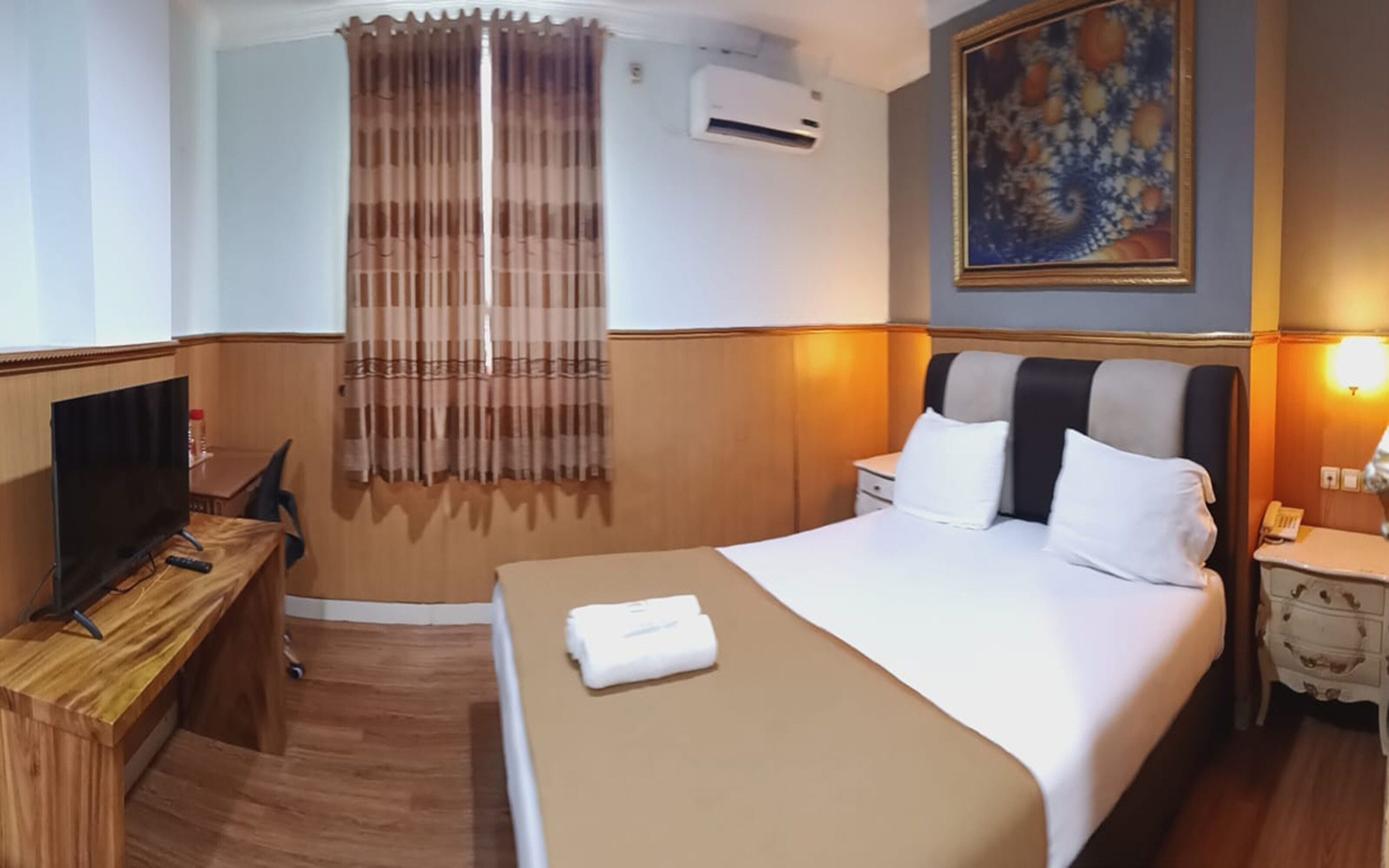 Ein Hotelzimmer mit Bett, Fernseher, Schreibtisch und einem Bild an der Wand.
