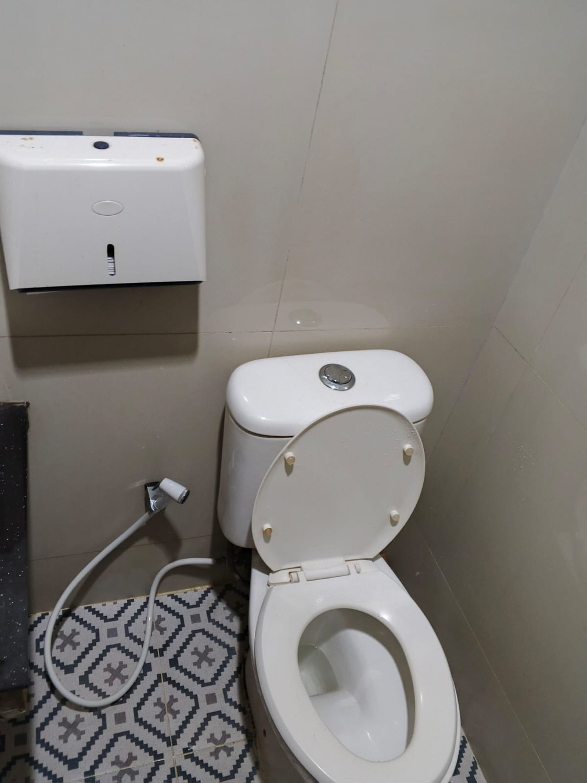 Un inodoro con asiento bidé, un suelo estampado y un dispensador de toallas de papel instalado en la pared.