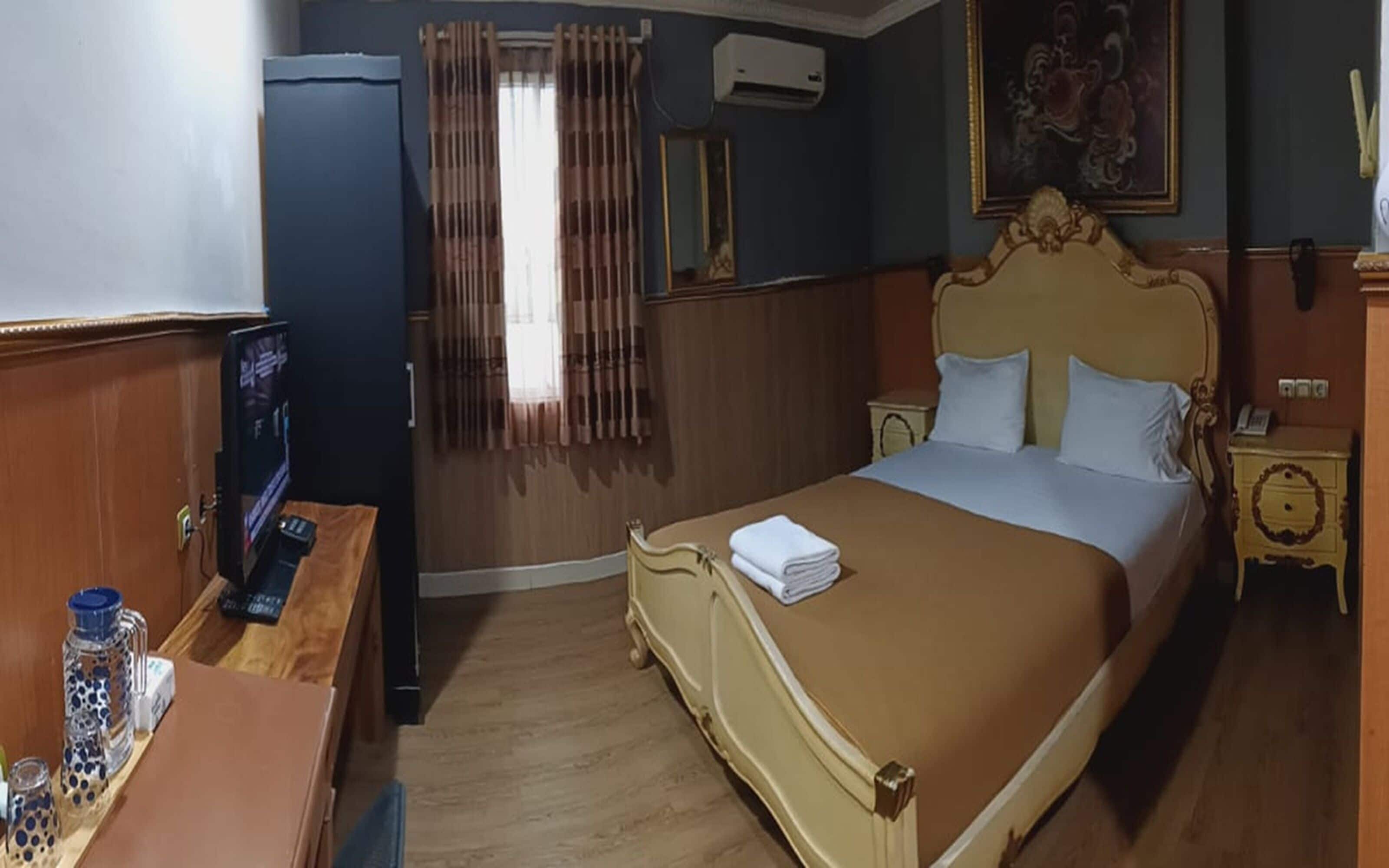 Quarto de hotel com cama, escrivaninha com computador, espelho e janela com cortinas.