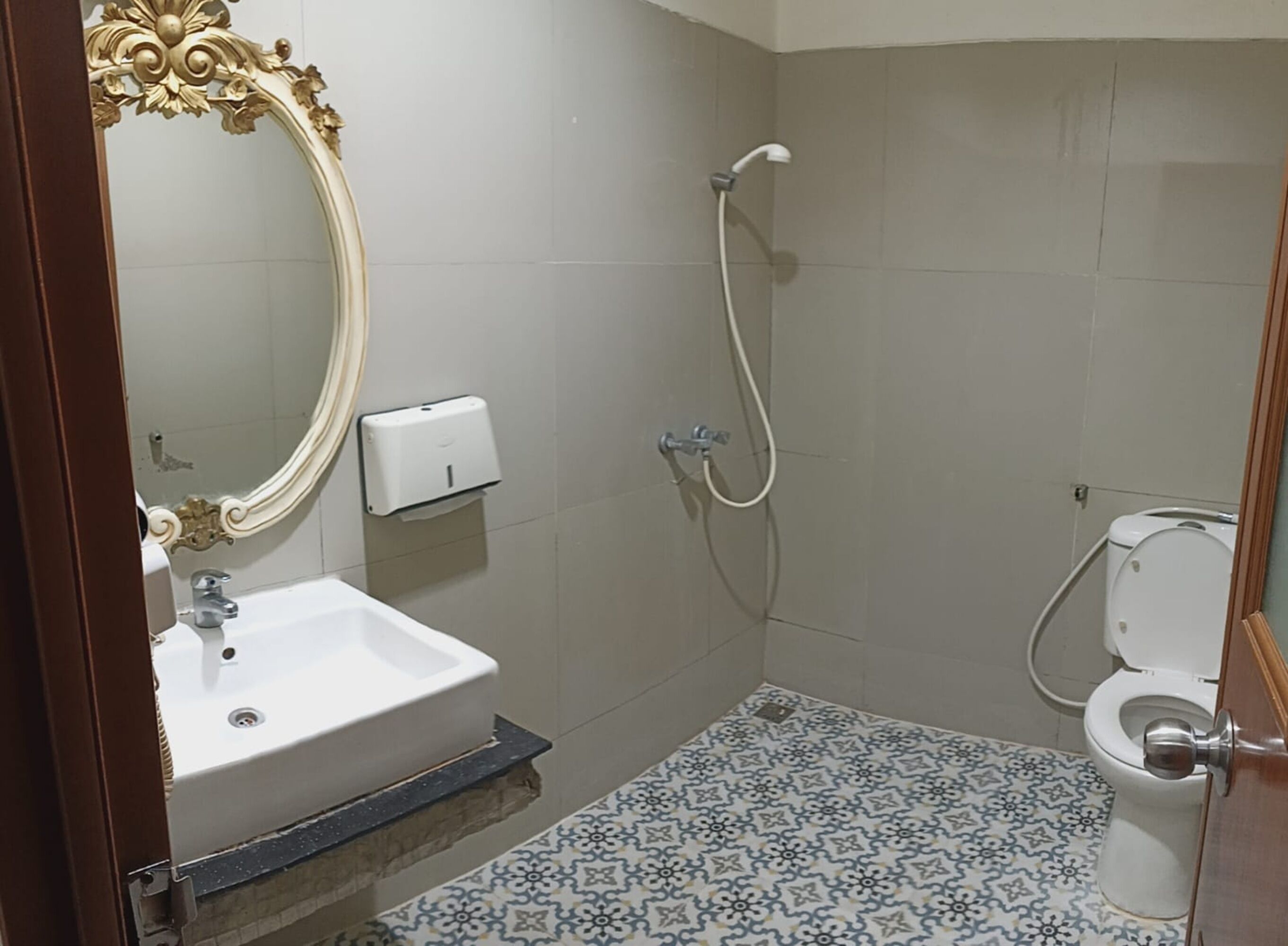 Ein Badezimmer mit einem weißen Waschbecken, einer Duschbrause, einer Toilette und einem Musterfliesenboden.