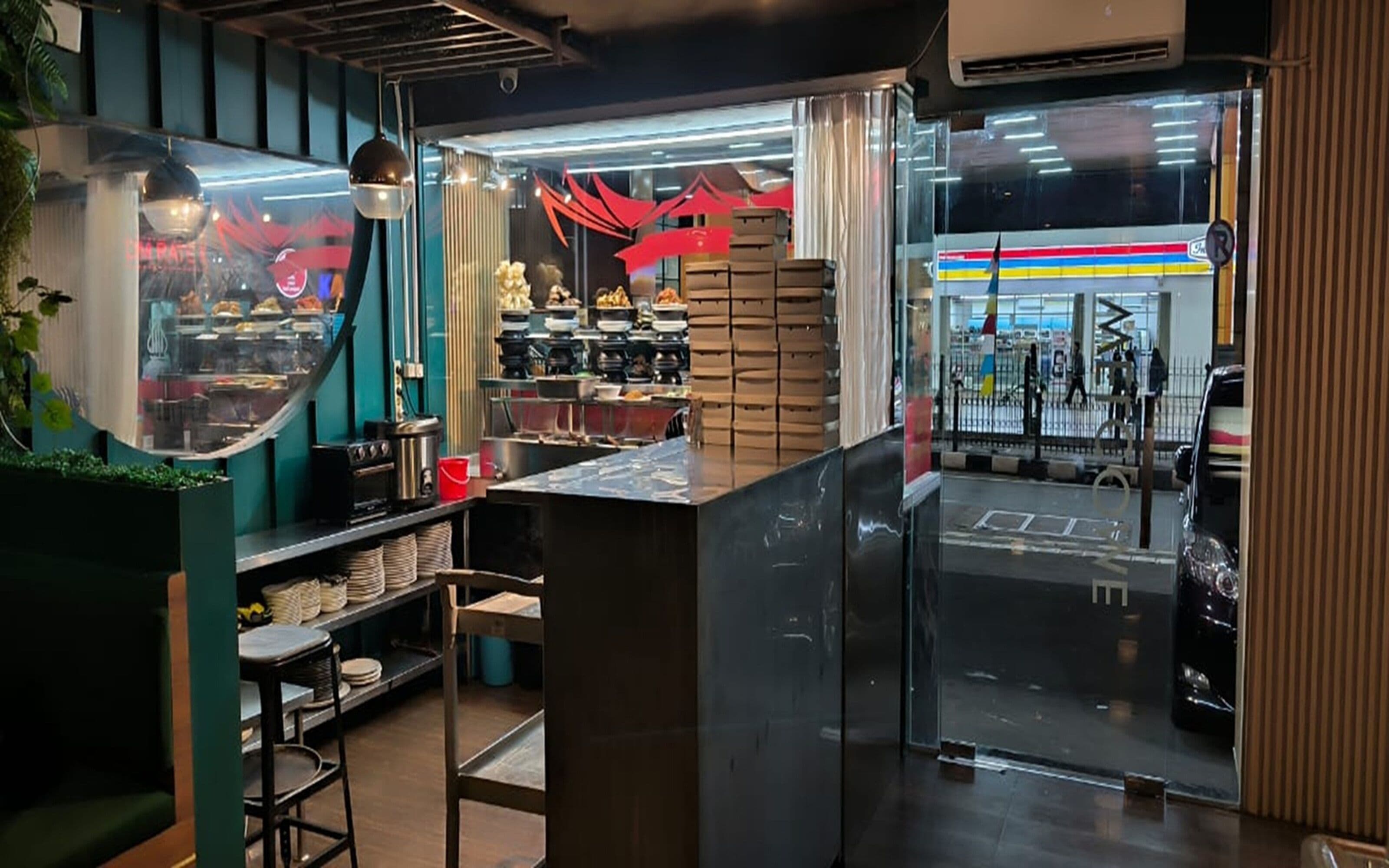 Un restaurante con mostrador, estantes con vajilla y vista a la calle.