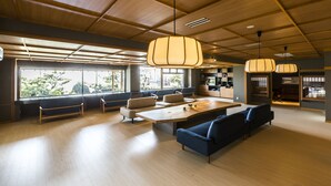 A spacious, modern interior with wooden flooring, a large dining table, comfortable seating, and large windows providing natural light. - Wakamatsu Chita Hot Spring Resort  (Minamichita)