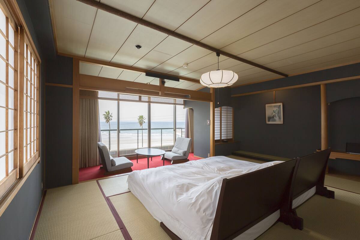 A hotel room with tatami flooring, a bed, a desk, and a view of the ocean.