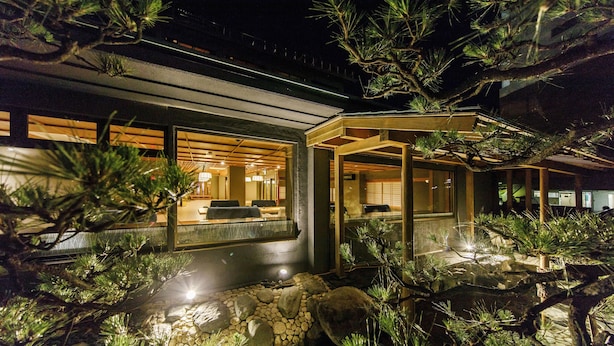 A modern house with a well-lit interior, a stone pathway, and pine trees. - Wakamatsu Chita Hot Spring Resort  (Minamichita)