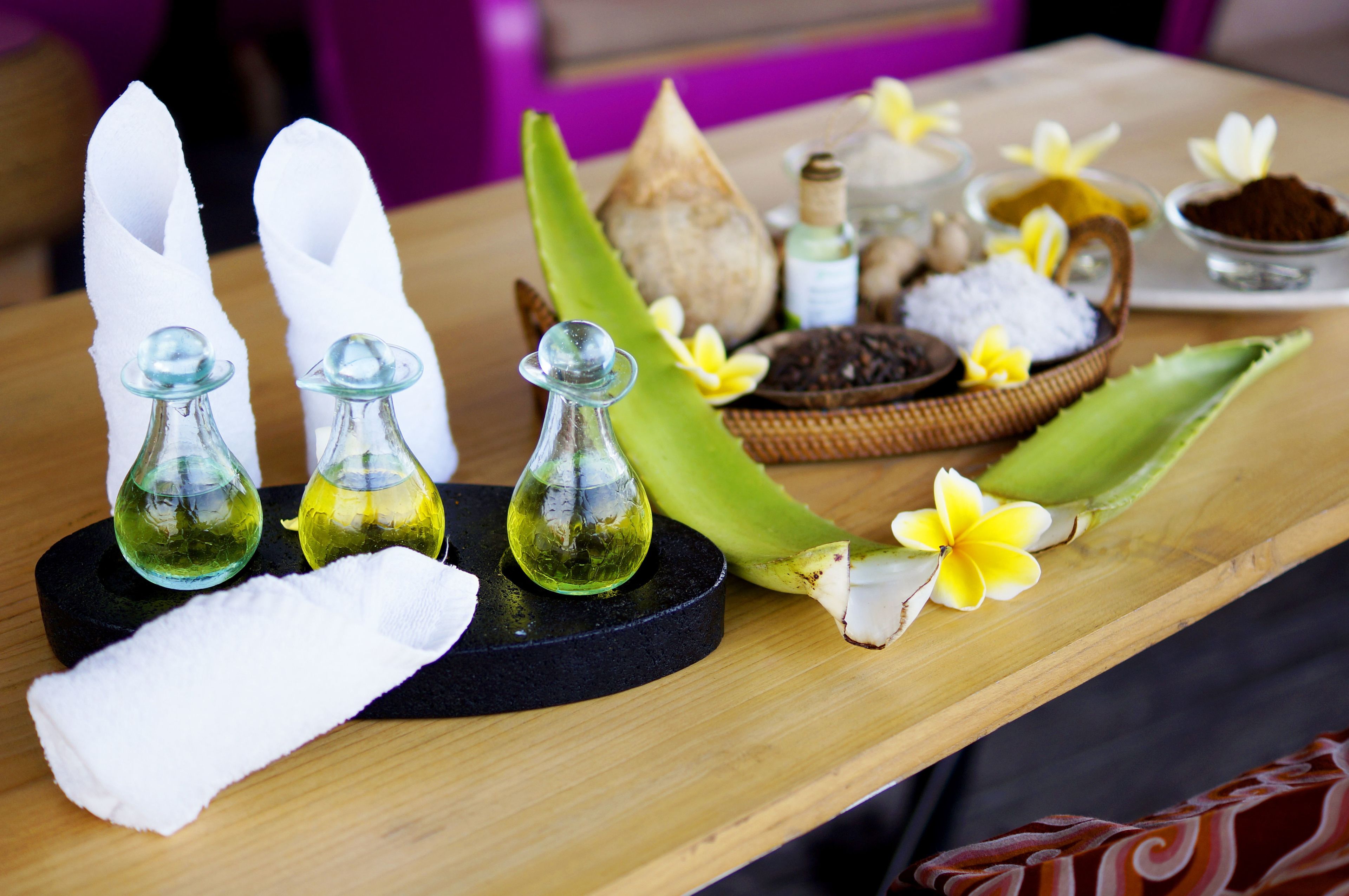 A wooden table with various spa products, including bottles of oil, a coconut, and a bowl of spices.