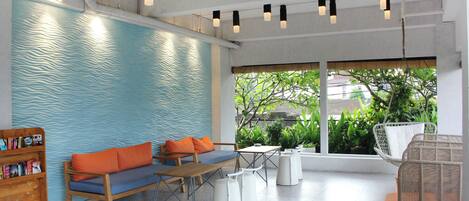 A modern indoor seating area with a blue textured wall, wooden furniture, and a view of greenery outside.