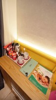 Una mesa de madera con una bandeja que contiene bocadillos, un termo y una cuchara. También hay folletos y un menú sobre la mesa.