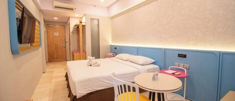 A hotel room with a bed, a small round table with a chair, a mirror, and a wall-mounted air conditioner.