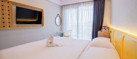 Habitación de hotel con una cama grande, un televisor de pantalla plana montado en la pared, una mesita redonda con una silla y una ventana con cortinas.