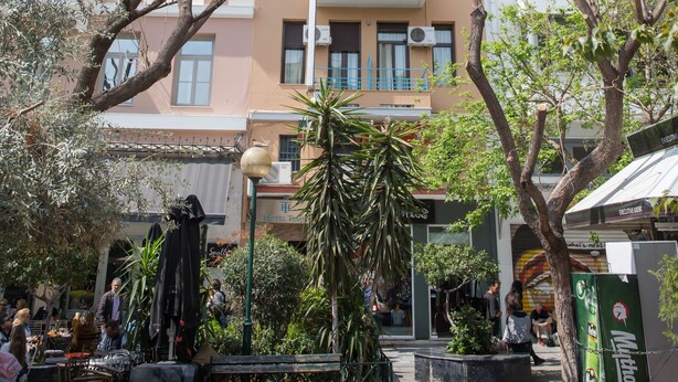 A multi-story building with balconies, a cafe area with outdoor seating, and a street with pedestrians. - Tempi Hotel (Athens)