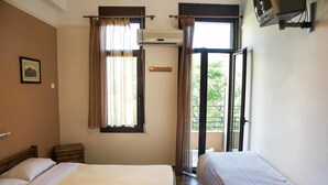 A hotel room with two beds, a window with curtains, an air conditioning unit, a small table, and a picture on the wall. - Tempi Hotel (Athens)