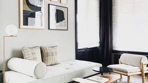 A modern living room with a sofa, armchairs, and a coffee table. There are framed pictures on the wall and a window with curtains. - Morgan and Mees Amsterdam (Amsterdam)