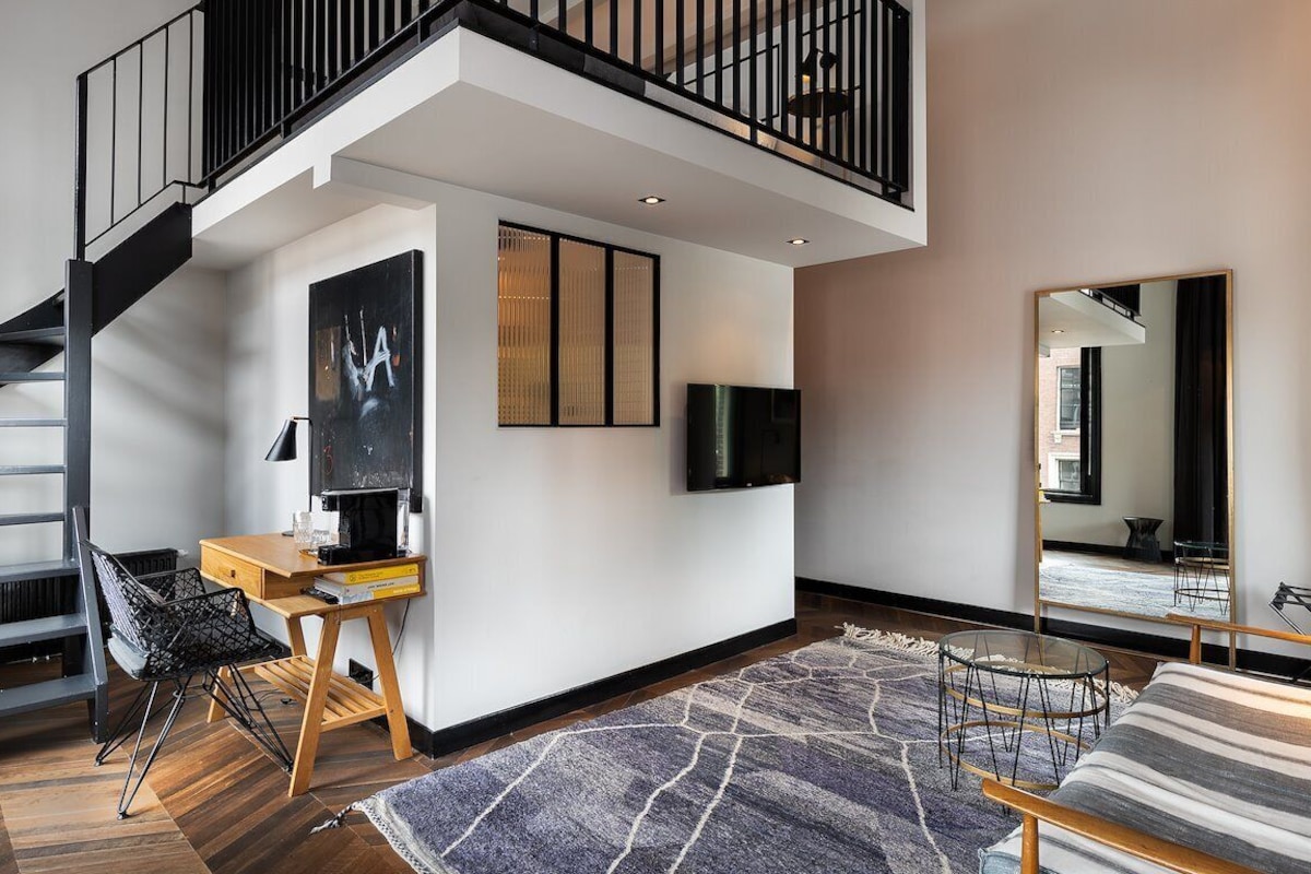 A modern living room with a staircase, a flat-screen TV, a wooden desk, and a sofa.