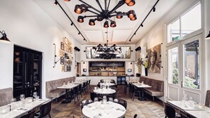 A restaurant with multiple dining tables and booths, a kitchen area in the center, and large windows providing natural light.