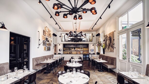 A restaurant with multiple dining tables and booths, a kitchen area in the center, and large windows providing natural light. - Morgan and Mees Amsterdam (Amsterdam)