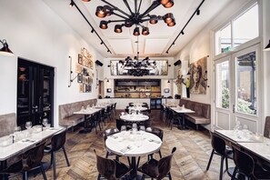 A restaurant with multiple dining tables and booths, a kitchen area in the center, and large windows providing natural light. -  Morgan and Mees Amsterdam (Amsterdam)