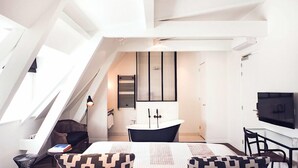 A modern, well-lit room with a sloped ceiling, a large bed, a black bathtub, a TV, and a desk with a chair. - Morgan and Mees Amsterdam (Amsterdam)