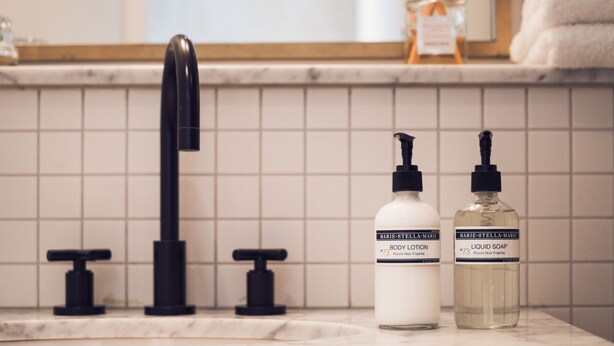 A bathroom with a marble countertop, a black faucet, and two bottles of Marie-Stella-Maris body lotion and liquid soap.