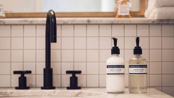 A bathroom with a marble countertop, a black faucet, and two bottles of Marie-Stella-Maris body lotion and liquid soap.