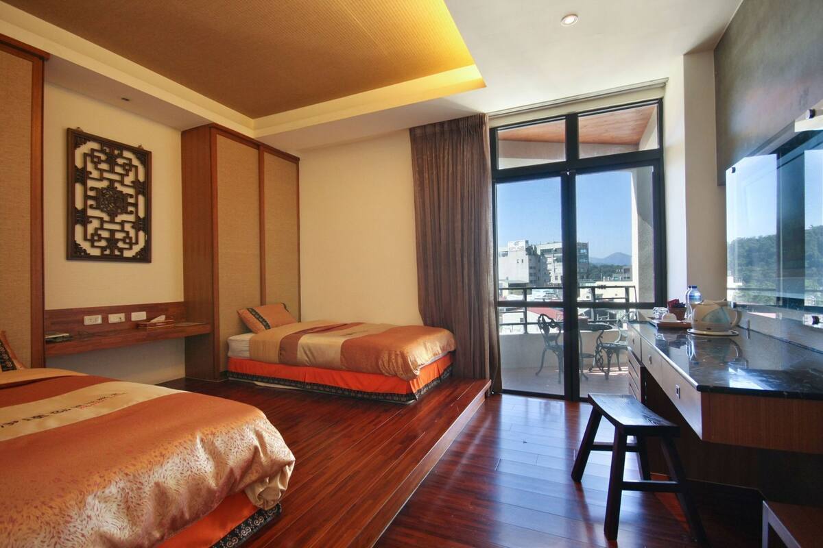 Une chambre d’hôtel avec deux lits, un balcon offrant une vue, un bureau et une grande fenêtre.