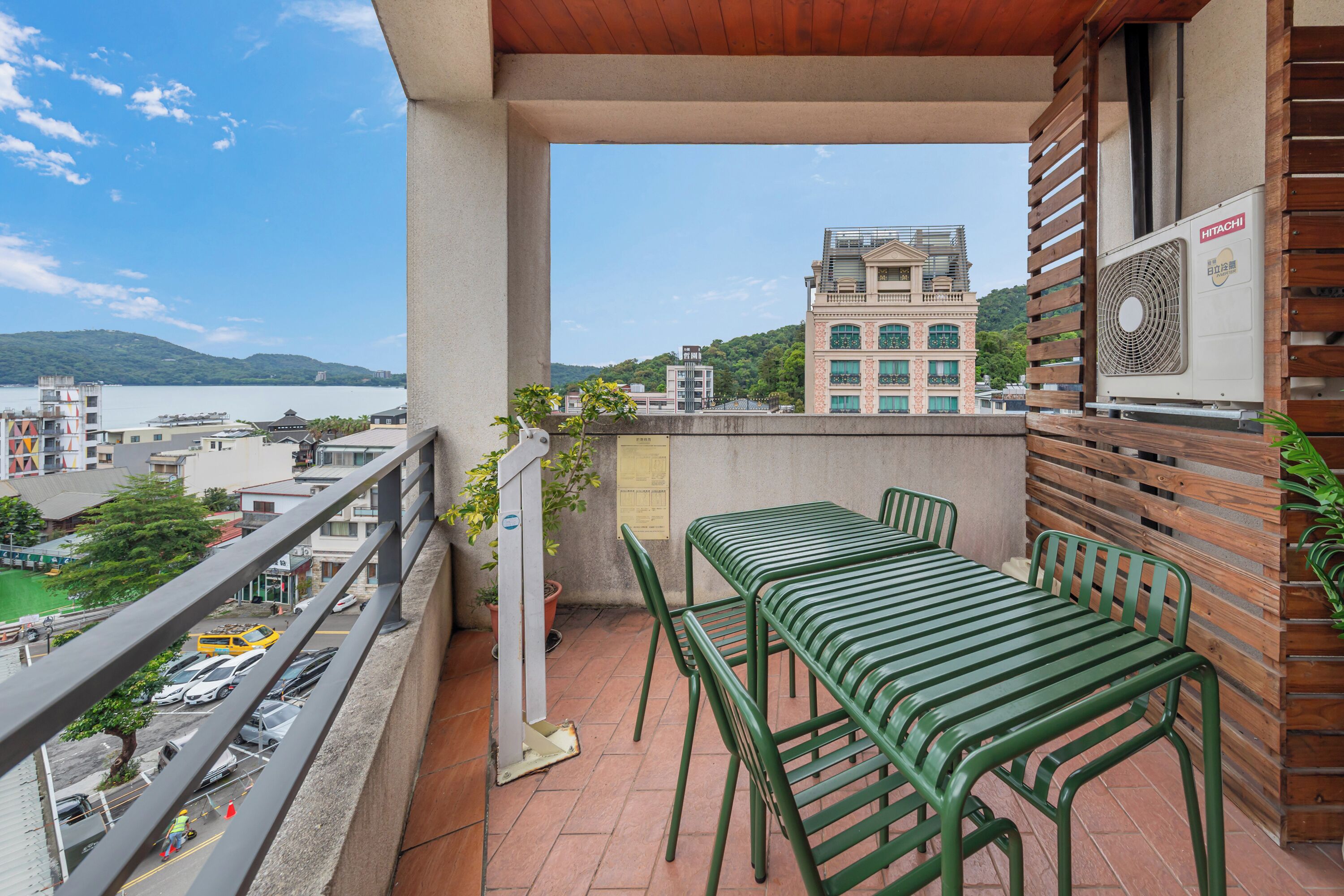A balcony with a table and chairs, overlooking a cityscape with buildings and a body of water.