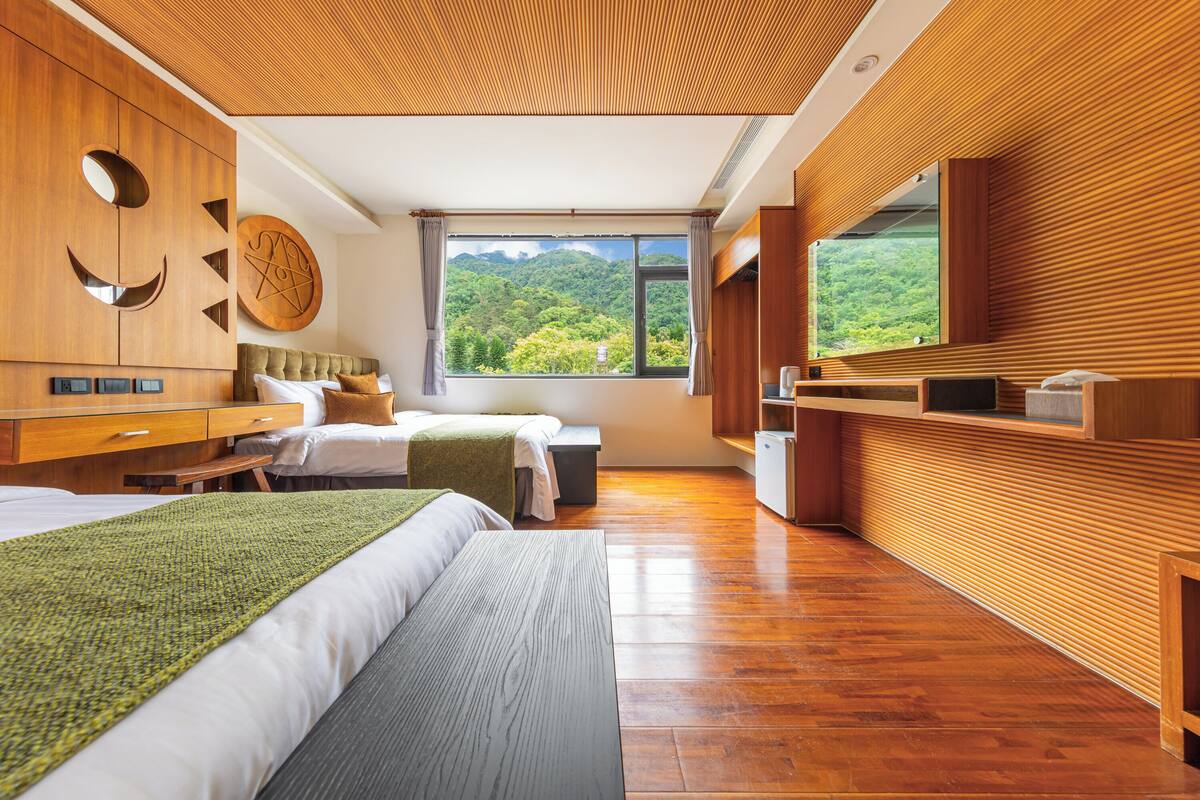Une chambre moderne avec un grand lit, un plus petit lit, des murs en bois, une grande fenêtre donnant sur les montagnes et une armoire en bois.