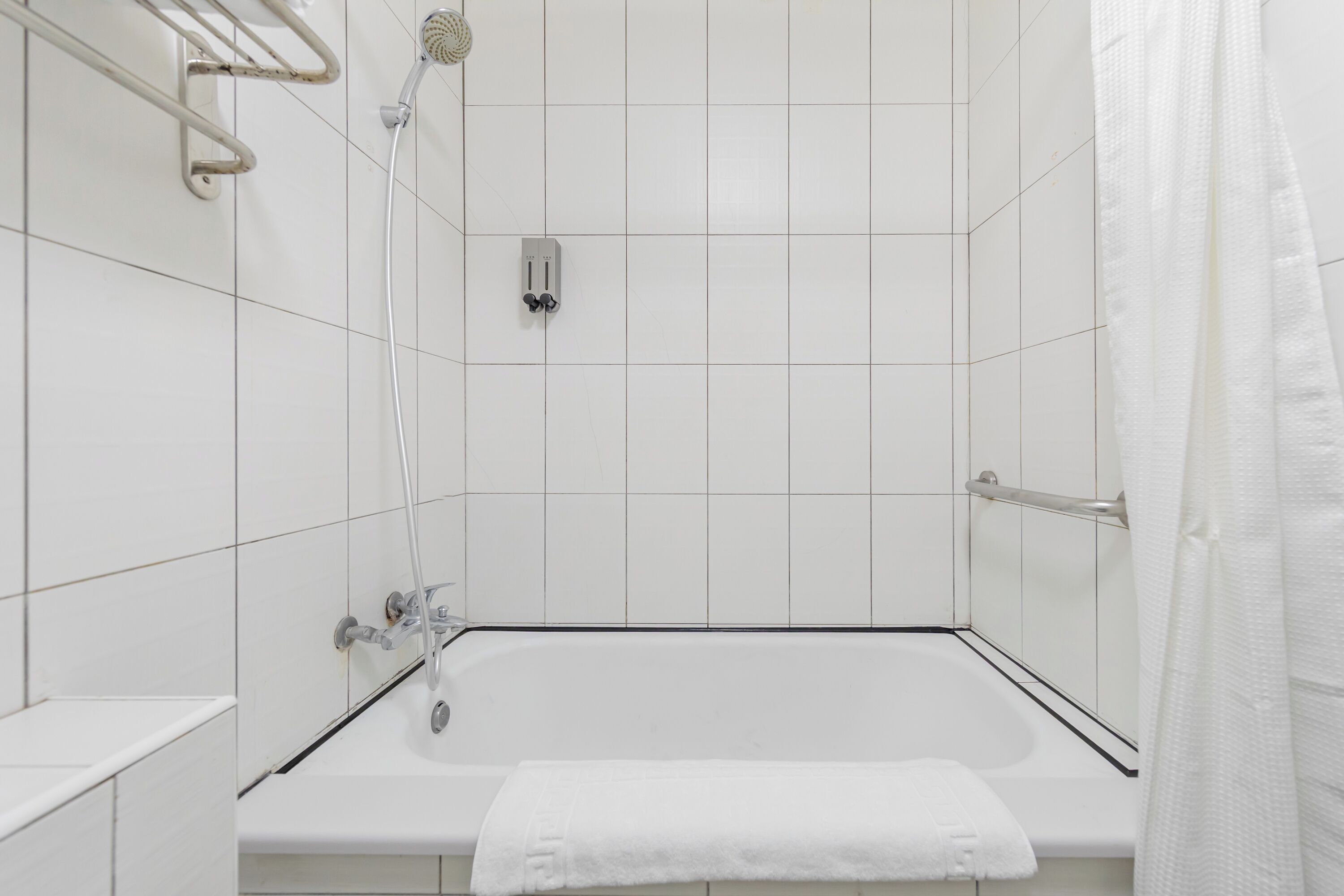 A modern bathroom with white tiles, a bathtub, a showerhead, and a towel rack.