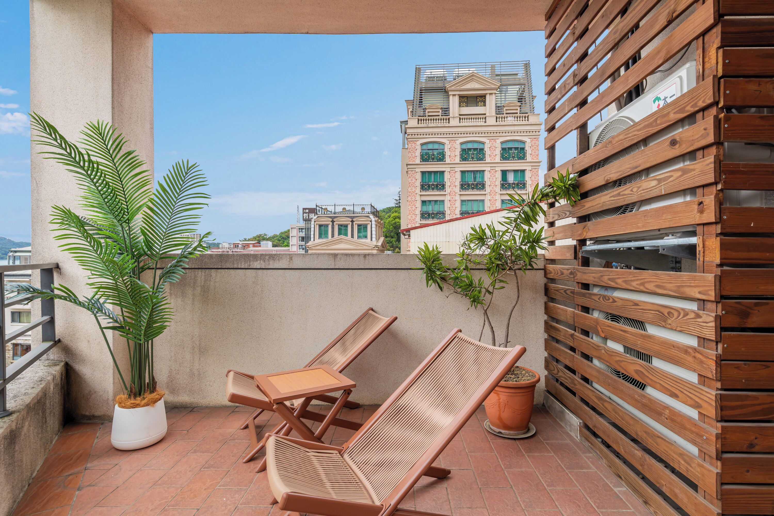 A balcony with two wooden lounge chairs, a potted plant, and a wooden fence.