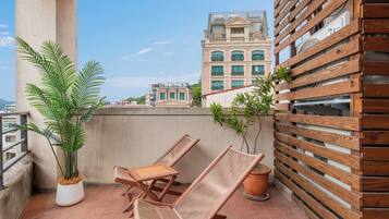 A balcony with two wooden lounge chairs, a potted plant, and a wooden fence.