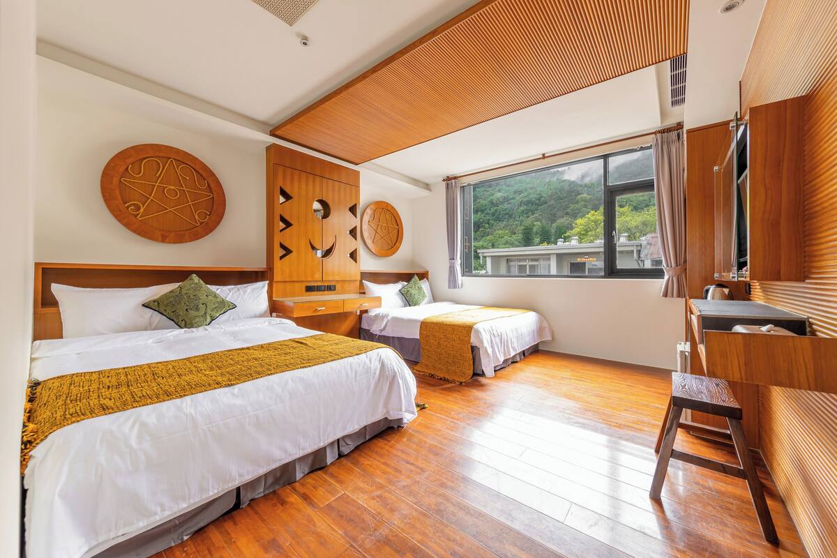 Une chambre d’hôtel avec deux lits, un plancher en bois, une grande fenêtre donnant sur un paysage verdoyant et un plafond en bois.