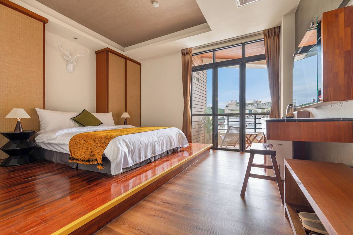 Une chambre d’hôtel avec un lit, des lampes de chevet, un bureau et une vue sur l’extérieur.